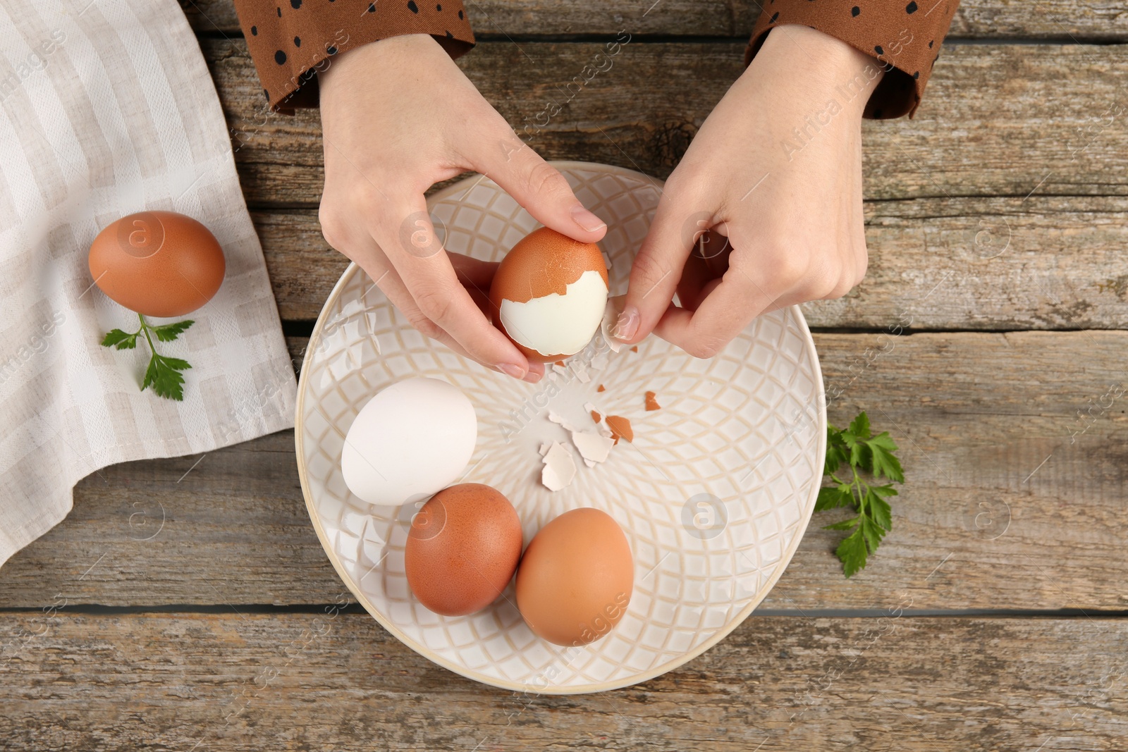Photo of Woman peeling boiled egg at old wooden table, top view