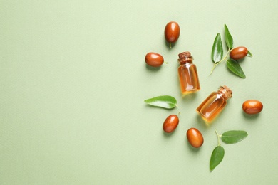 Photo of Glass bottles with jojoba oil and seeds on green background, flat lay. Space for text
