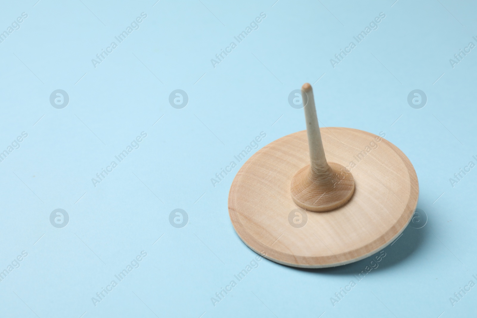 Photo of One wooden spinning top on light blue background, closeup. Space for text