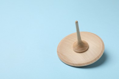 One wooden spinning top on light blue background, closeup. Space for text