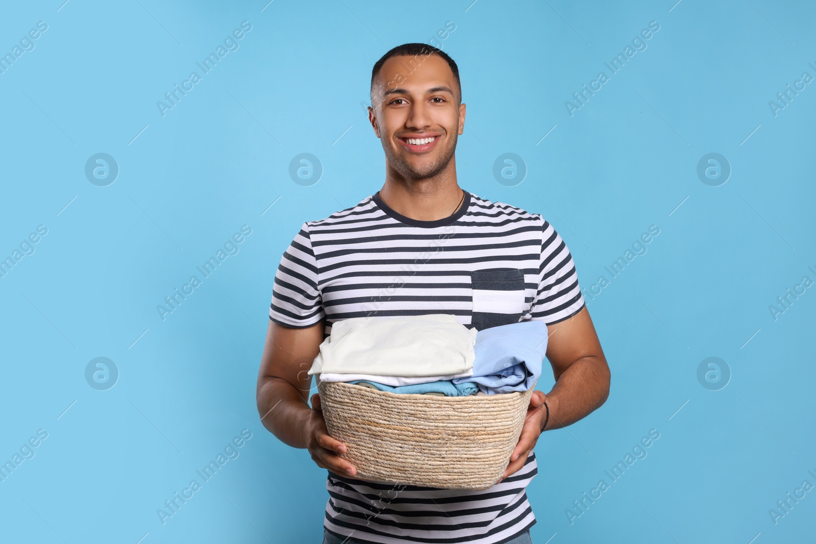 Photo of Happy man with basket full of laundry on light blue background