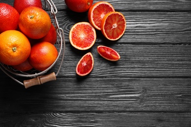 Photo of Whole and cut red oranges on black wooden table, flat lay. Space for text