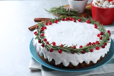 Traditional Christmas cake decorated with rosemary and cranberries on light grey marble table