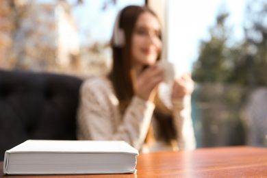 Photo of Book on table in cafe and woman with headphones on background. Audiobook concept