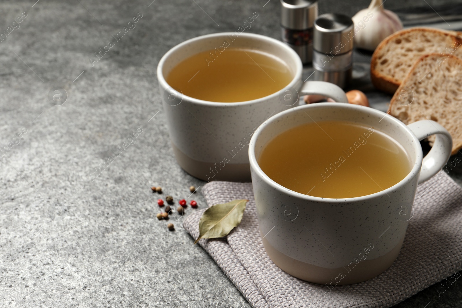 Photo of Hot delicious bouillon in cups on grey table. Space for text