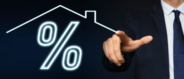 Image of Mortgage. Man drawing house roof and percent sign on virtual screen against dark blue background, closeup. Banner design