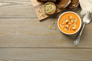 Photo of Tasty creamy pumpkin soup served with bread and seeds on wooden table, flat lay. Space for text