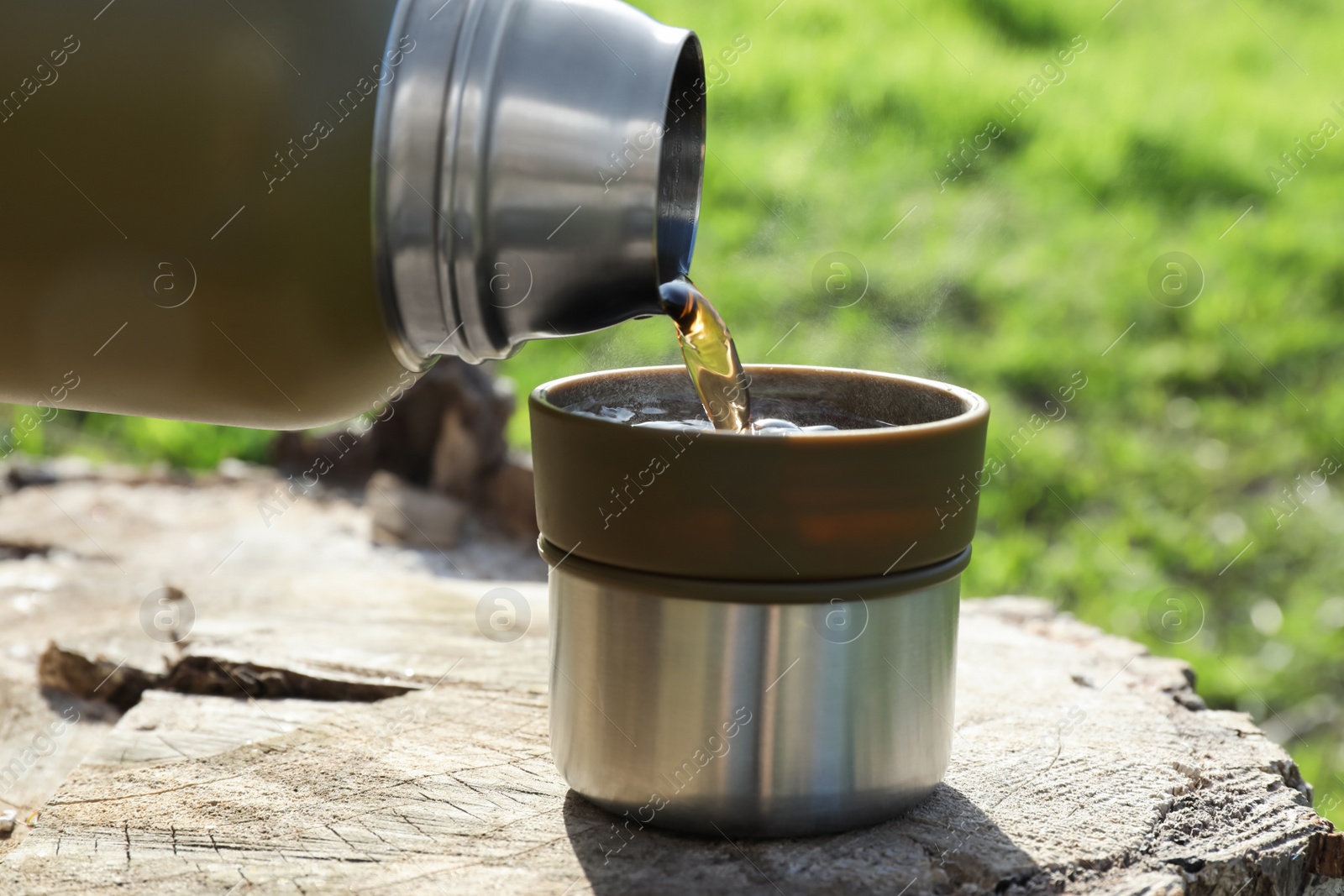 Photo of Pouring hot drink into mug on tree stump, closeup