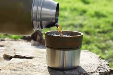 Pouring hot drink into mug on tree stump, closeup