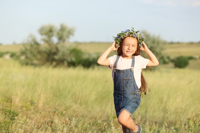 Cute little girl wearing flower wreath outdoors, space for text. Child spending time in nature