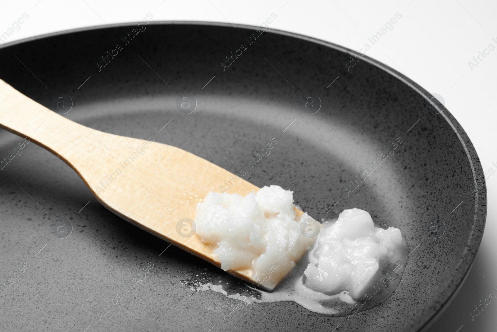 Photo of Frying pan with coconut oil and wooden spatula on white background, closeup. Healthy cooking