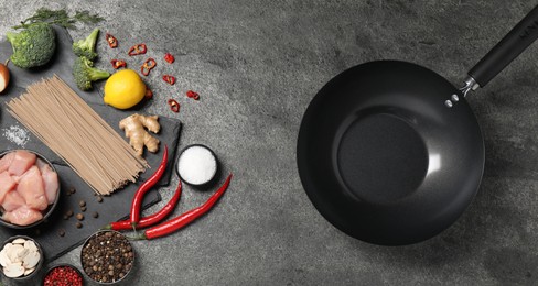 Empty iron wok and raw ingredients on grey table, flat lay