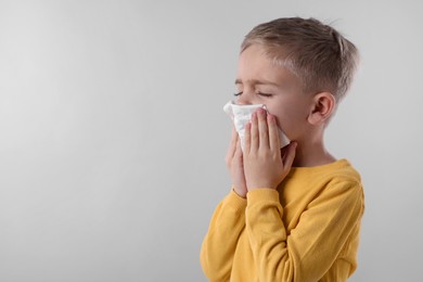 Photo of Sick boy with tissue coughing on gray background, space for text. Cold symptoms