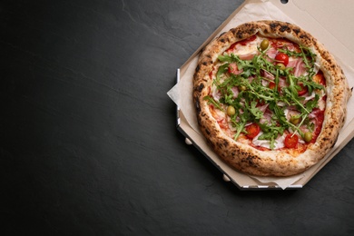 Tasty pizza with meat and arugula in cardboard box on black table, top view. Space for text