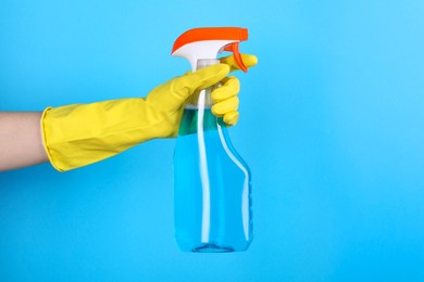 Photo of Woman holding plastic spray bottle on light blue background, closeup