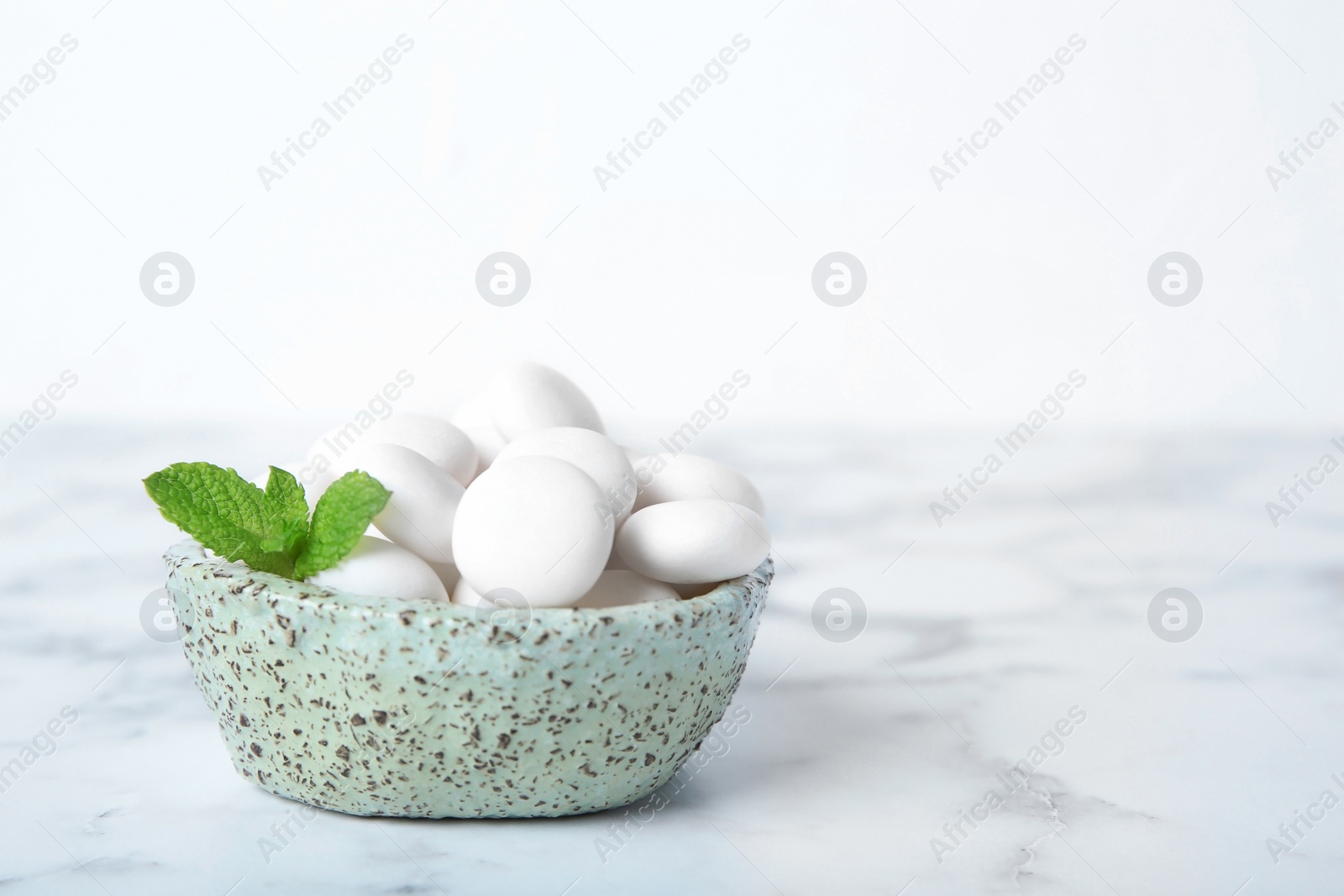 Photo of Bowl with tasty mint candies and leaves on table