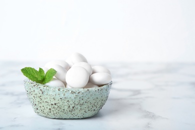 Bowl with tasty mint candies and leaves on table