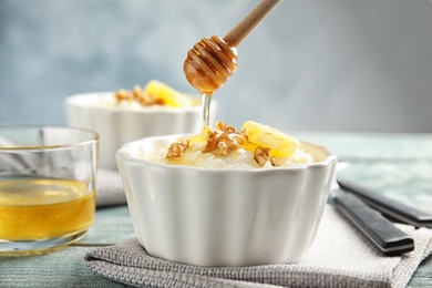 Photo of Pouring honey onto rice pudding with walnuts and orange slice in ramekin on table