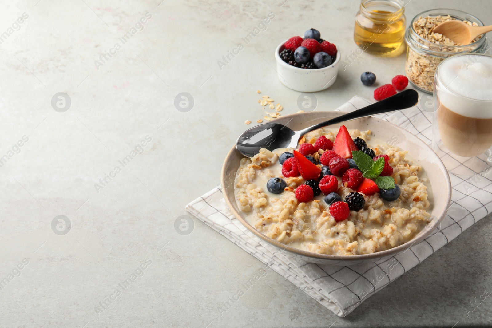 Photo of Bowl of oatmeal porridge served with berries on light grey table, space for text