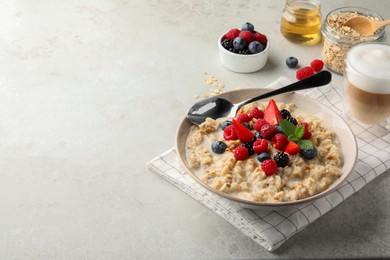 Photo of Bowl of oatmeal porridge served with berries on light grey table, space for text