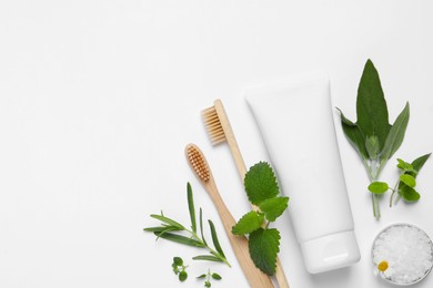 Bamboo toothbrushes, tube of cream, sea salt and herbs on white background, flat lay. Space for text