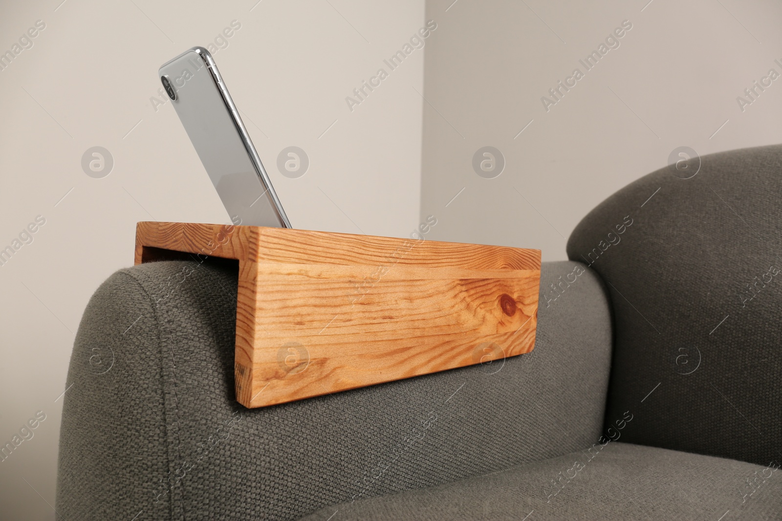 Photo of Smartphone on sofa with wooden armrest table in room. Interior element