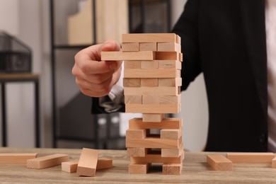 Playing Jenga. Man removing wooden block from tower at table indoors, closeup