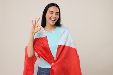 Photo of Happy young woman with flag of Canada showing OK gesture on beige background