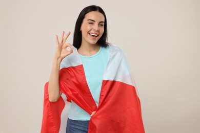 Happy young woman with flag of Canada showing OK gesture on beige background