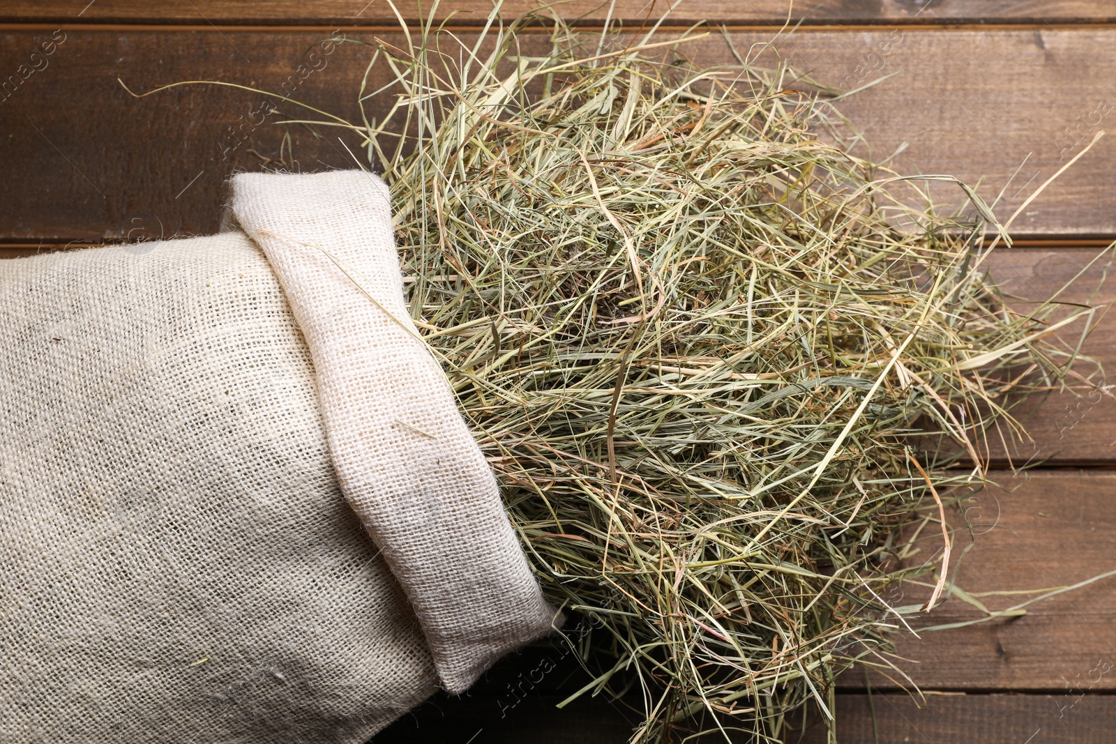 Photo of Dried hay in burlap sack on wooden table, top view