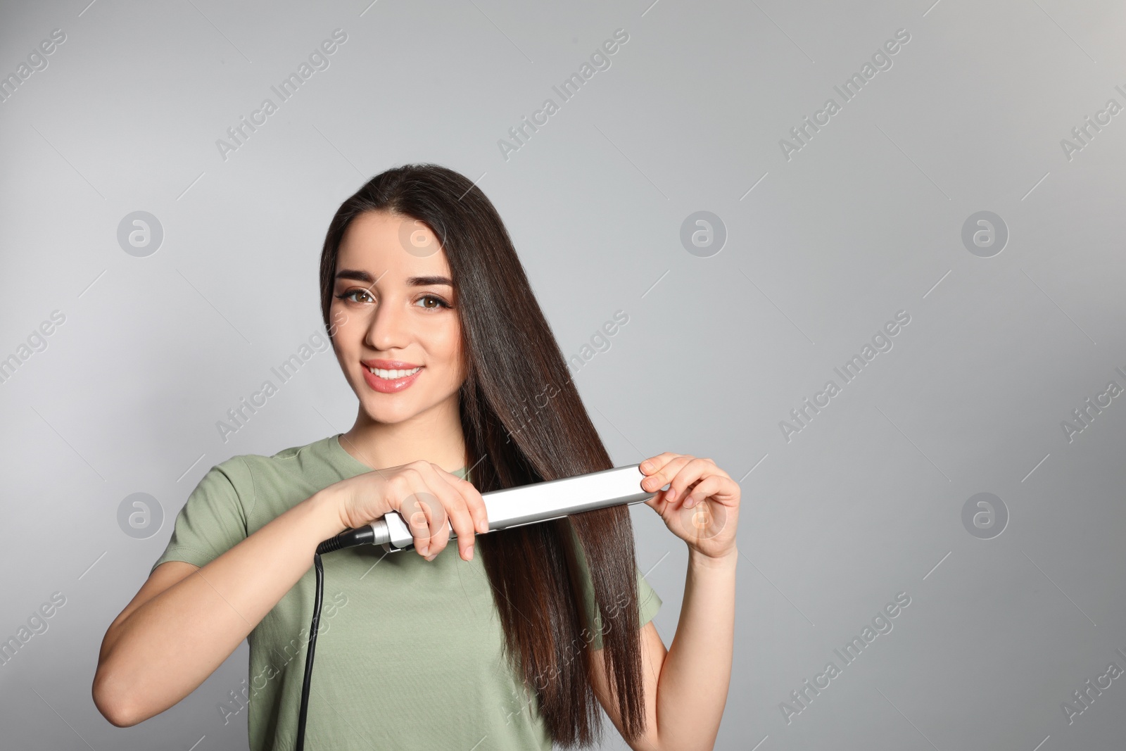 Photo of Happy woman using hair iron on grey background. Space for text