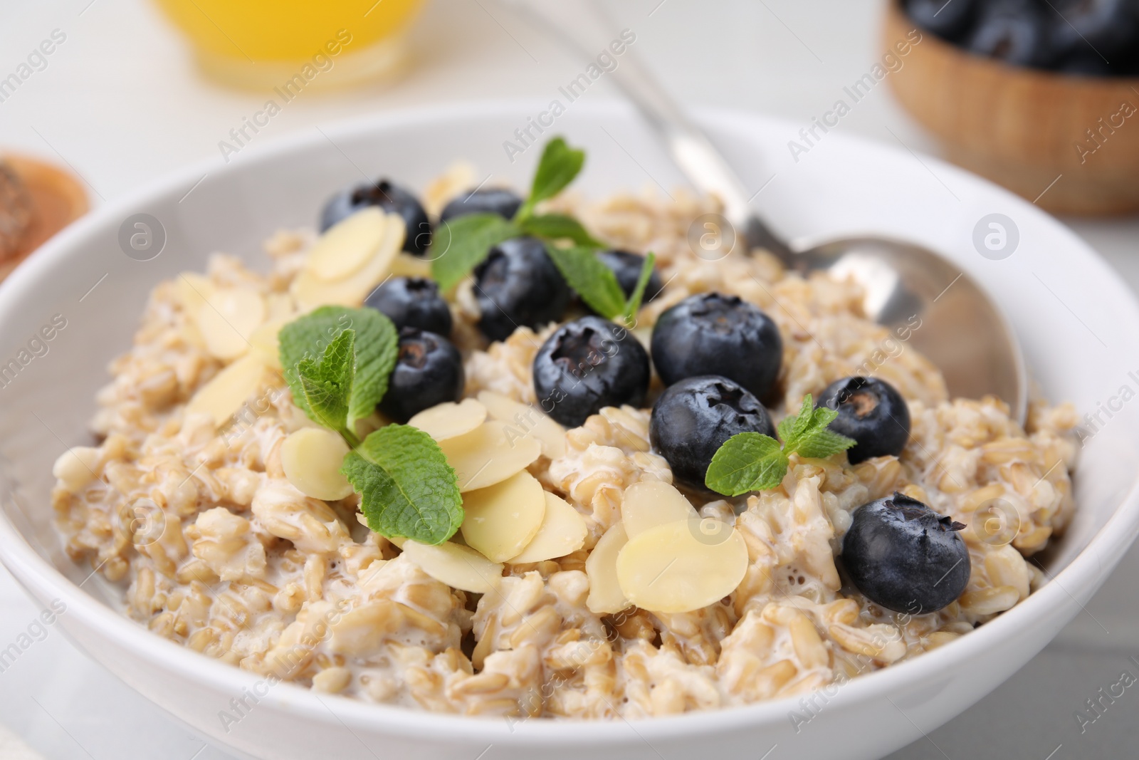 Photo of Tasty oatmeal with blueberries, mint and almond petals in bowl on white table, closeup