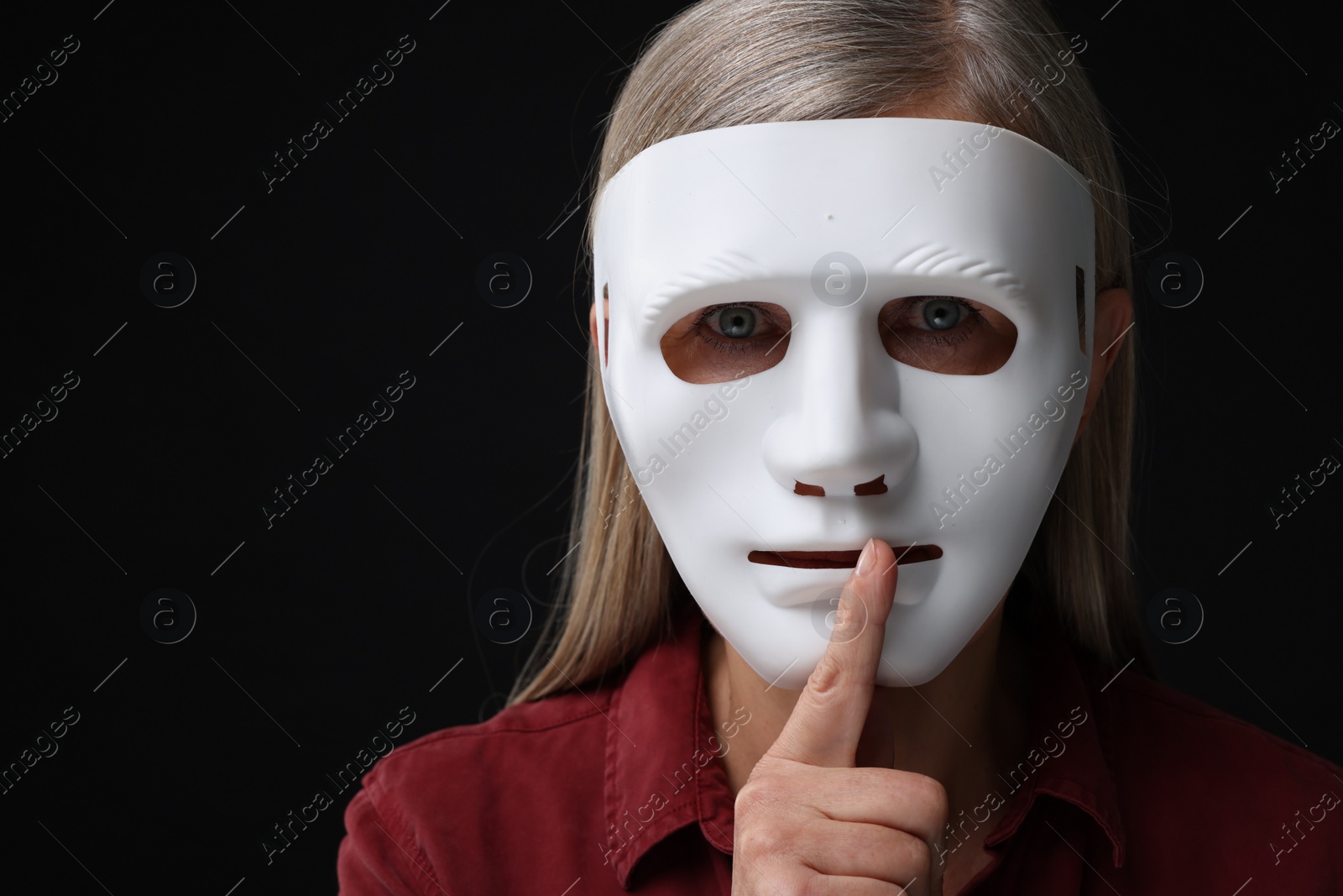 Photo of Multiple personality concept. Woman in mask showing hush gesture on black background, space for text