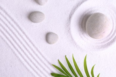 Photo of Zen garden stones and green leaves on white sand with pattern, flat lay