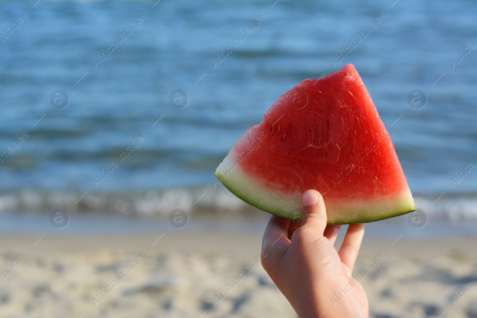 Photo of Child holding slice of fresh juicy watermelon near sea, closeup. Space for text