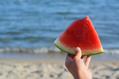 Child holding slice of fresh juicy watermelon near sea, closeup. Space for text