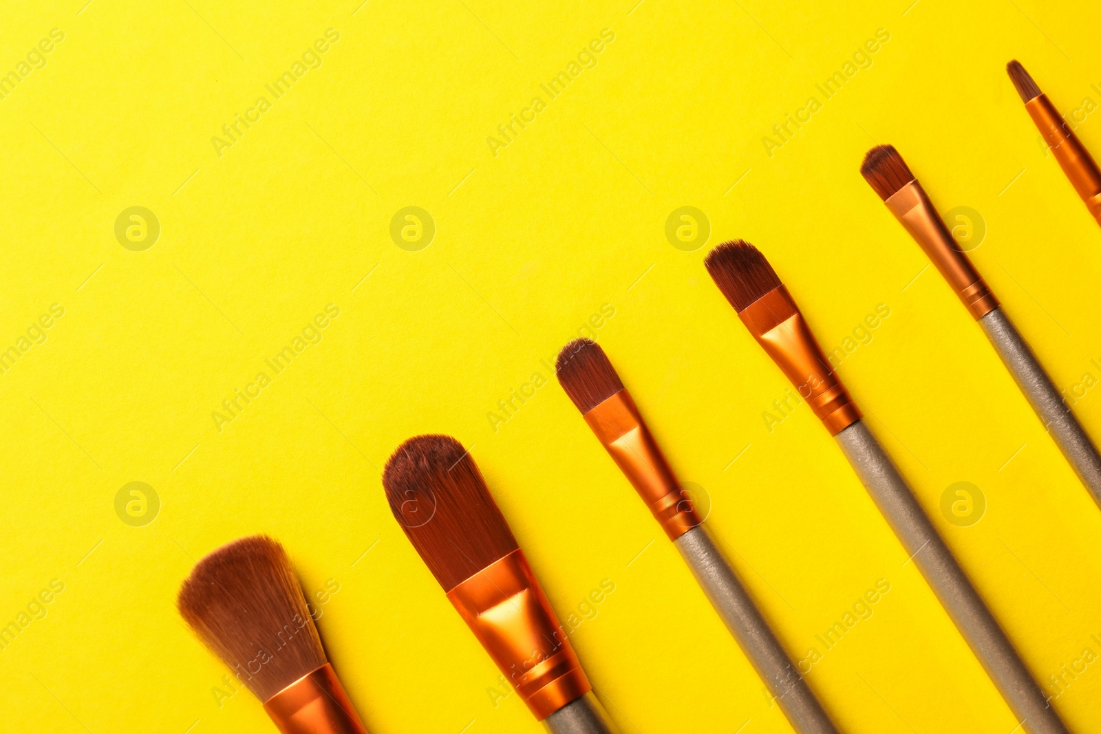 Photo of Different makeup brushes on yellow background, flat lay. Space for text