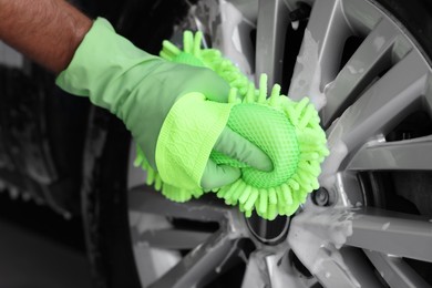 Photo of Worker washing car wheel with sponge, closeup