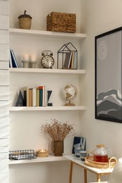 Photo of Books, alarm clock and different decor on shelves in room. Interior design