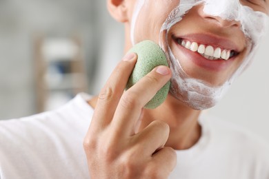 Photo of Happy young man washing off face mask with sponge in bathroom, closeup