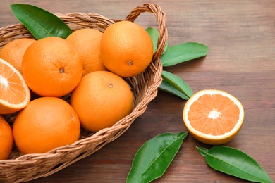 Photo of Wicker basket with ripe juicy oranges and green leaves on wooden table