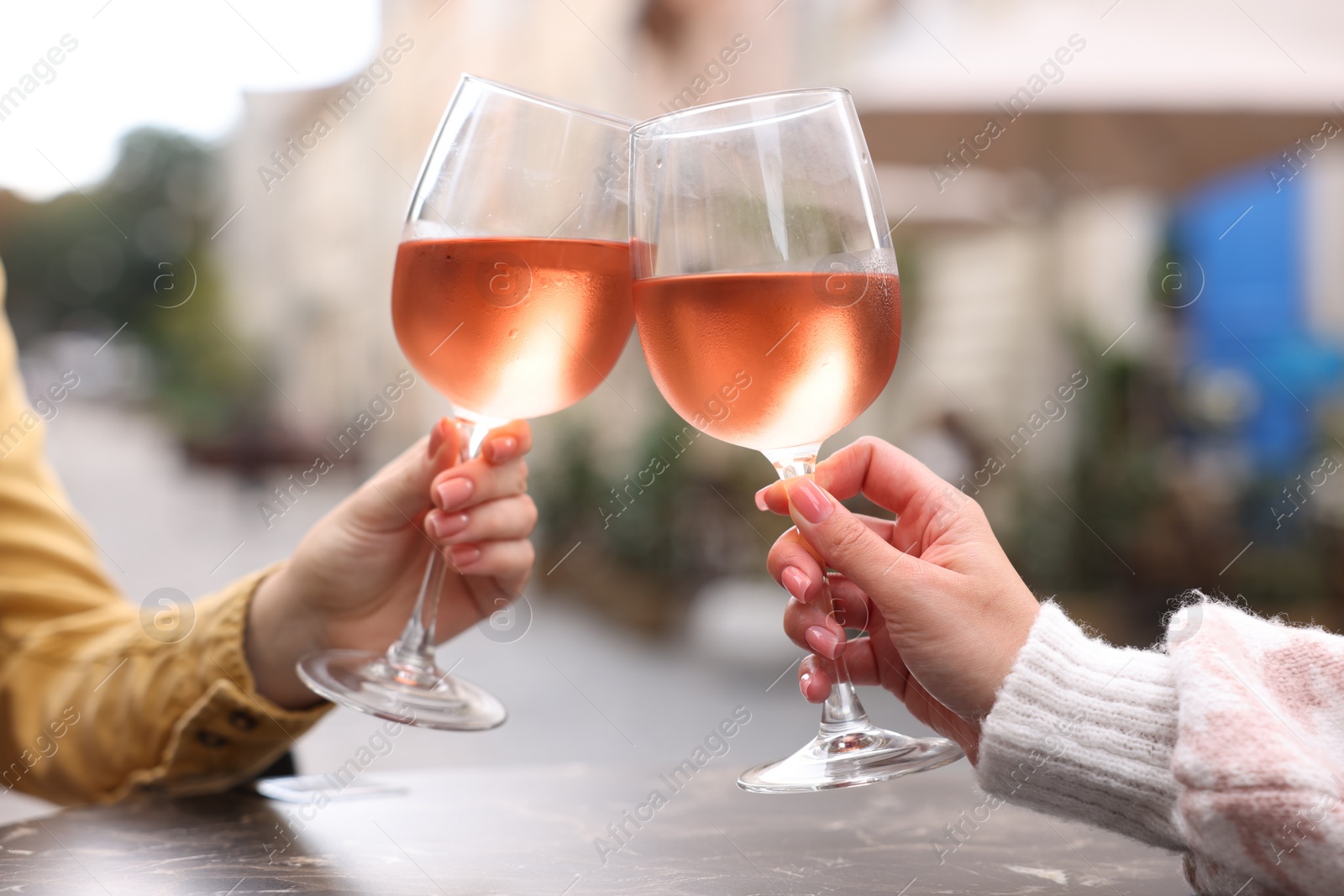 Photo of Women clinking glasses with rose wine at dark table in outdoor cafe, closeup