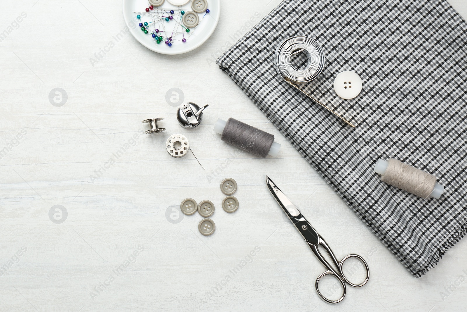 Photo of Flat lay composition with different sewing supplies and fabric on white wooden table. Space for text