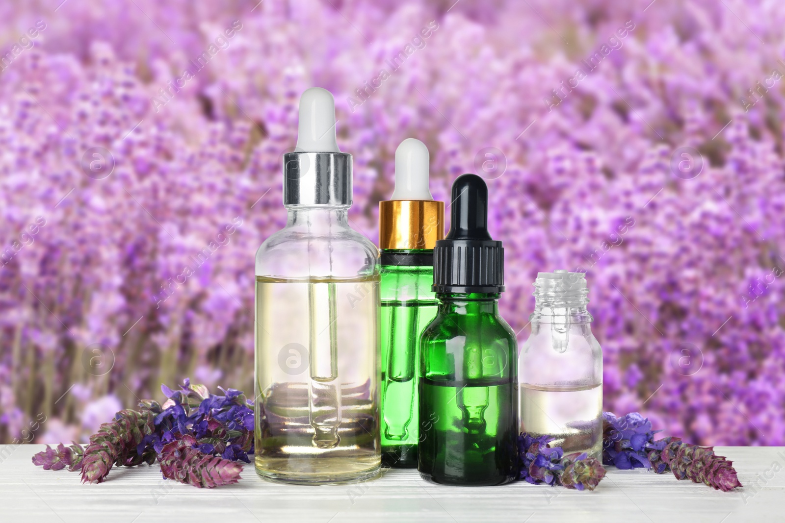Image of Bottles of essential oils and wildflowers on wooden table against blurred background
