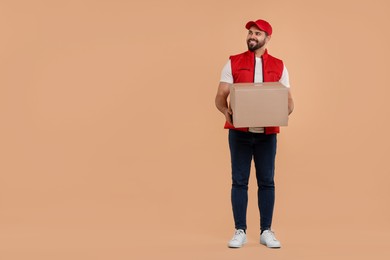 Photo of Happy young courier with parcel on light brown background, space for text