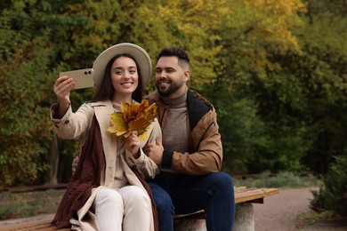 Happy young couple taking selfie in autumn park, space for text