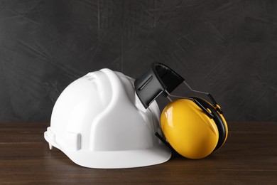 Photo of Hard hat and earmuffs on wooden table. Safety equipment