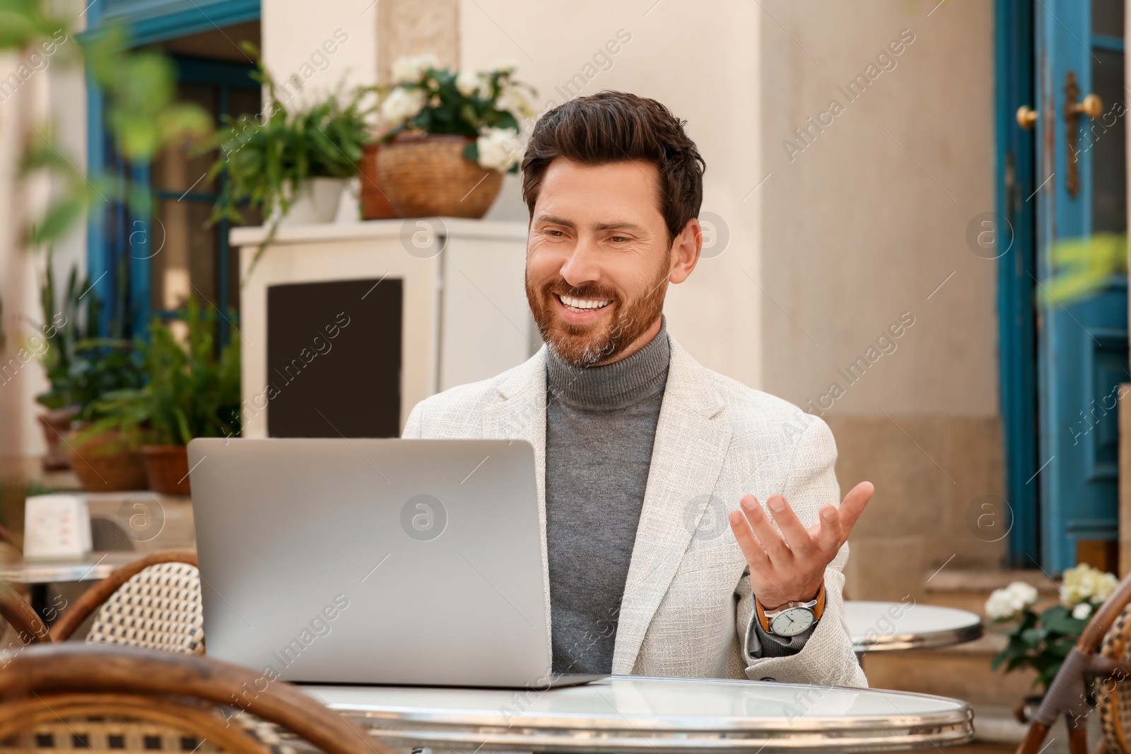 Photo of Man having video chat via laptop at table in outdoor cafe