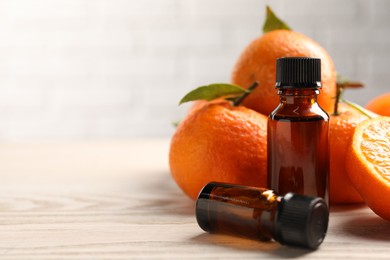 Photo of Bottles of tangerine essential oil and fresh fruits on wooden table, closeup. Space for text