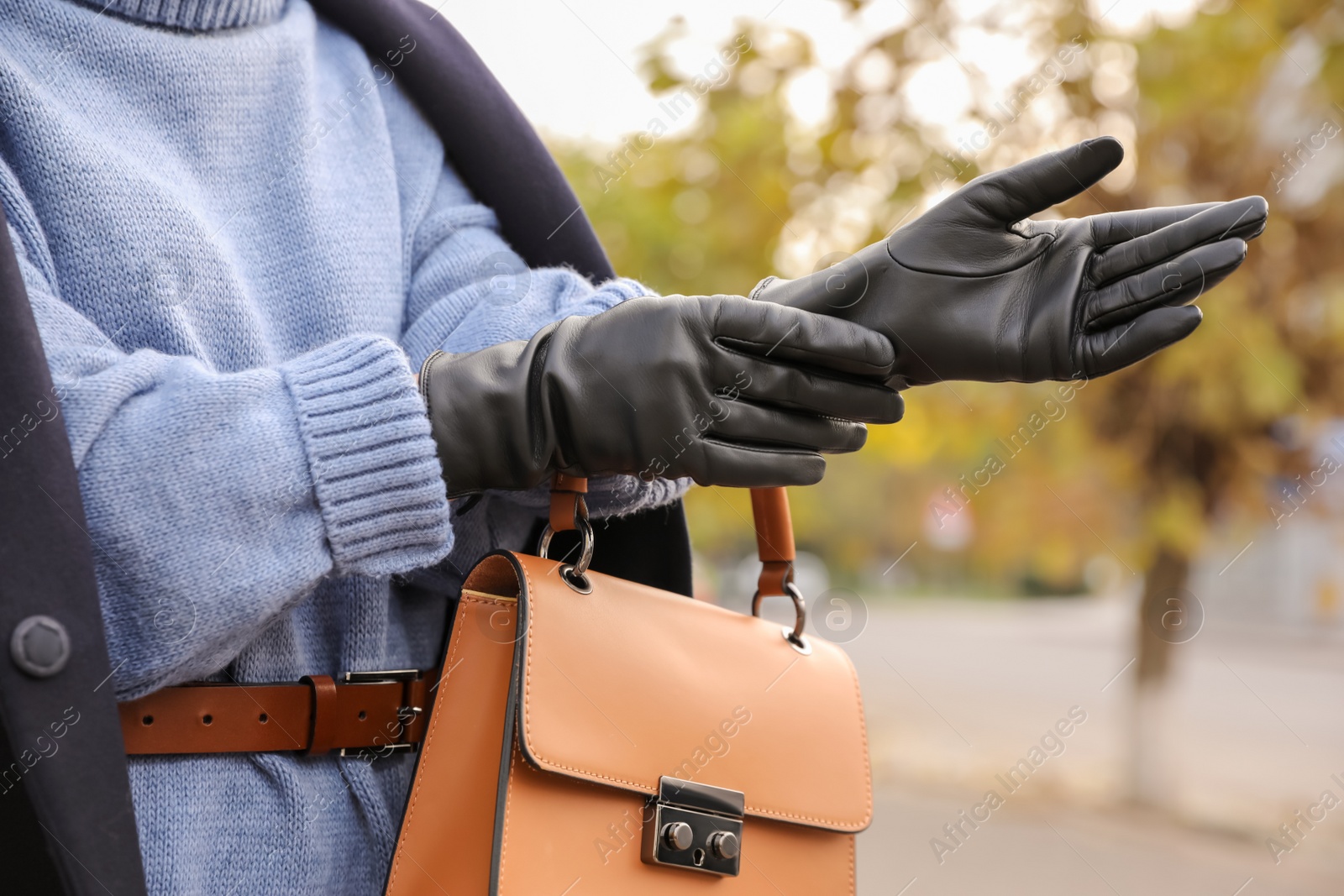 Photo of Young woman putting on stylish black leather gloves outdoors, closeup